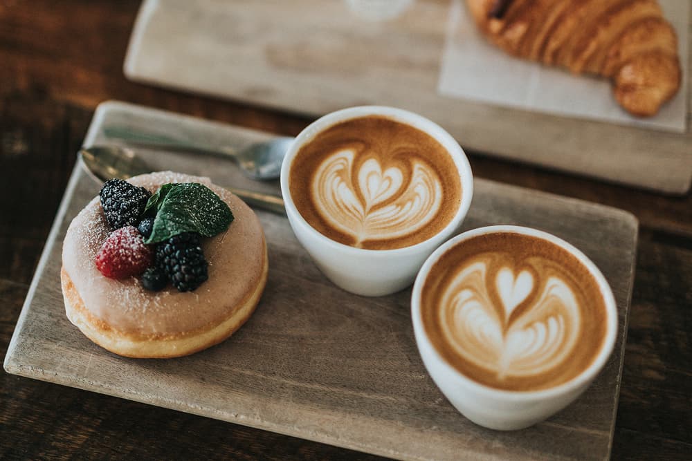 Deux tasses de latte art sont posées à côté d'un beignet garni de baies et d'un croissant.