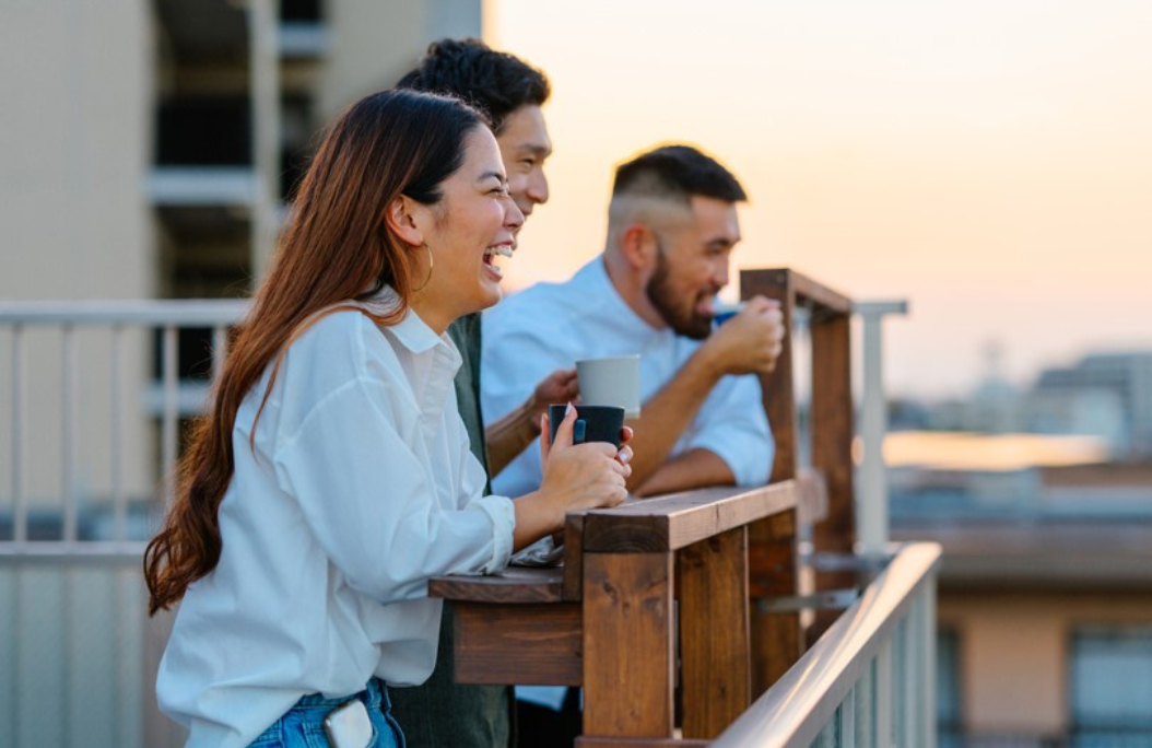A group of friends enjoys coffee on a balcony, overlooking the city against a sunset backdrop. Warm and relaxed atmosphere