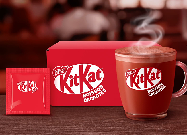 Boisson cacaotée KitKat dans une tasse transparente avec boîte rouge et sachet assorti.