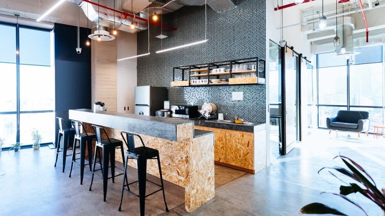 Cuisine moderne avec un bar en béton, des tabourets noirs et un mur en mosaïque, dotée de grandes fenêtres.