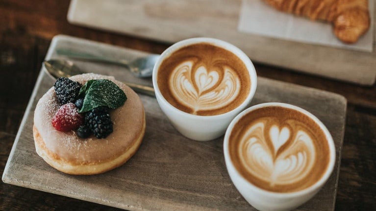 Deux tasses de latte art sont posées à côté d'un beignet garni de baies et d'un croissant.