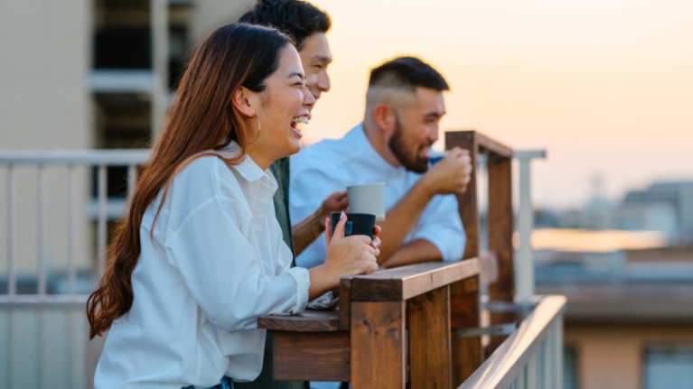 A group of friends enjoys coffee on a balcony, overlooking the city against a sunset backdrop. Warm and relaxed atmosphere