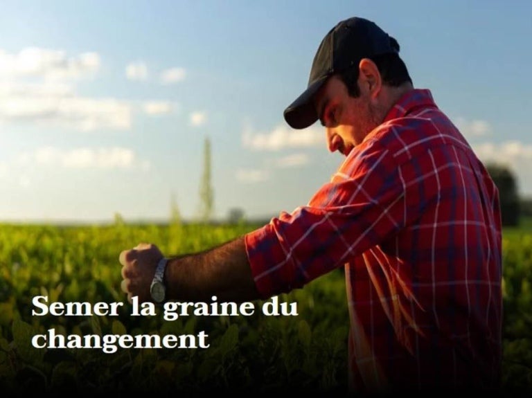 A person in a red plaid shirt gestures towards a lush green field under a blue sky, symbolizing change and growth