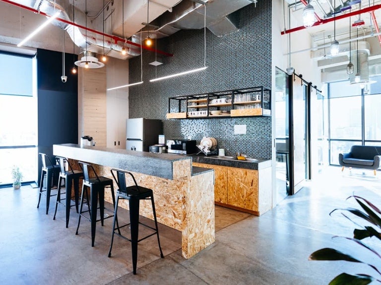 Cuisine moderne avec un bar en béton, des tabourets noirs et un mur en mosaïque, dotée de grandes fenêtres.