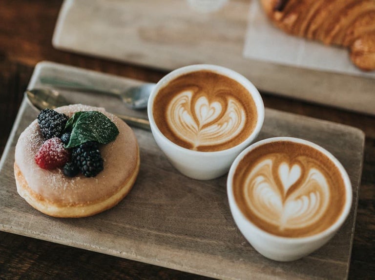 Deux tasses de latte art sont posées à côté d'un beignet garni de baies et d'un croissant.