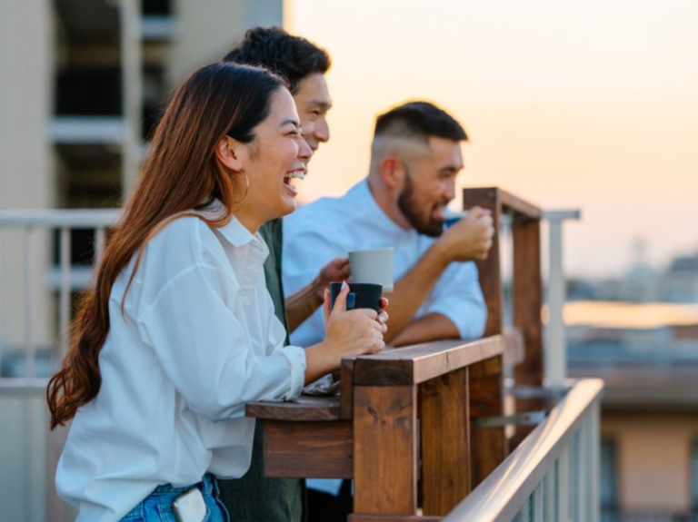 A group of friends enjoys coffee on a balcony, overlooking the city against a sunset backdrop. Warm and relaxed atmosphere