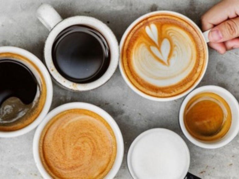 An assortment of coffee cups, including espresso, black coffee, and latte art, with a hand holding one cup