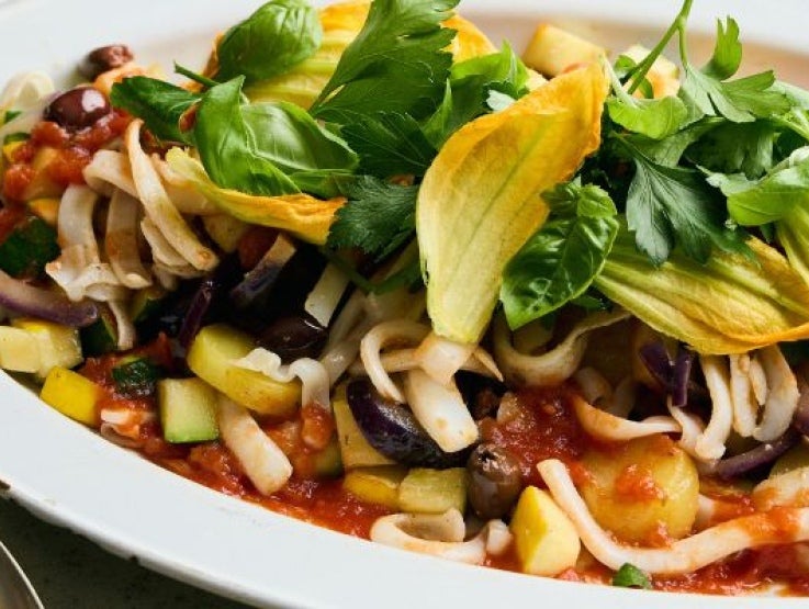 A vibrant plate of pasta with zucchini, eggplant, olives, and a garnish of fresh greens, drizzled with tomato sauce.