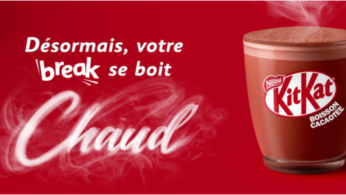 A steaming cup of KitKat hot chocolate against a red background, promoting a cozy break with the slogan "Chaud" (Hot).
